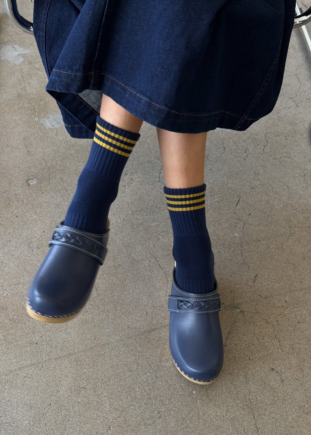 Person wearing navy clogs and socks with yellow stripes on a concrete floor.