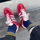 Red sneakers with white laces and blue socks with yellow stripes on a concrete surface.
