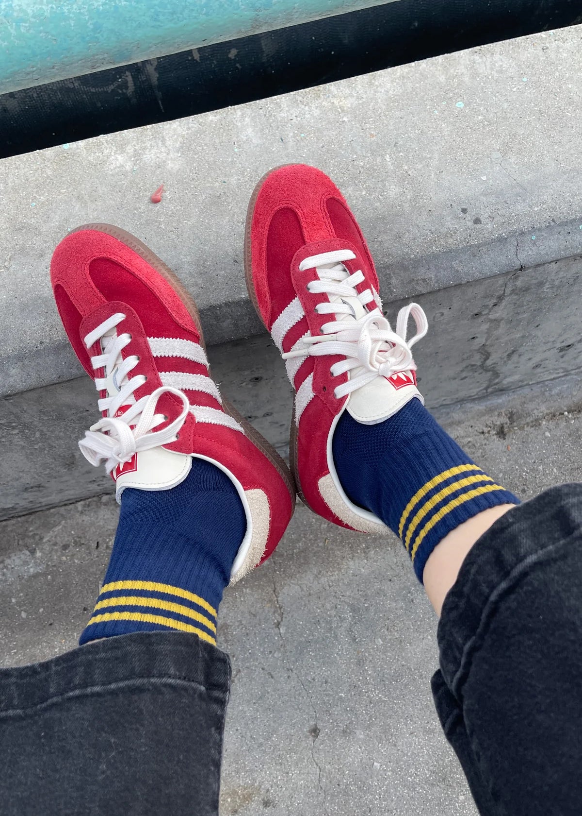 Red sneakers with white laces and blue socks with yellow stripes on a concrete surface.