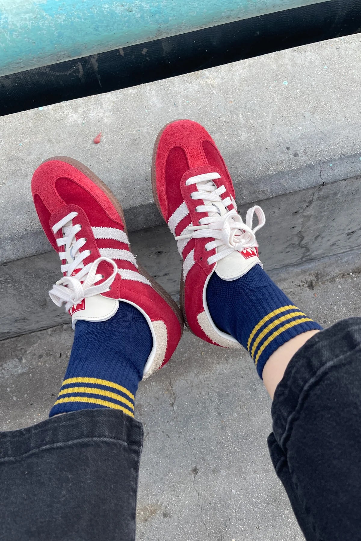 Red sneakers with white laces and blue socks with yellow stripes on a concrete surface.
