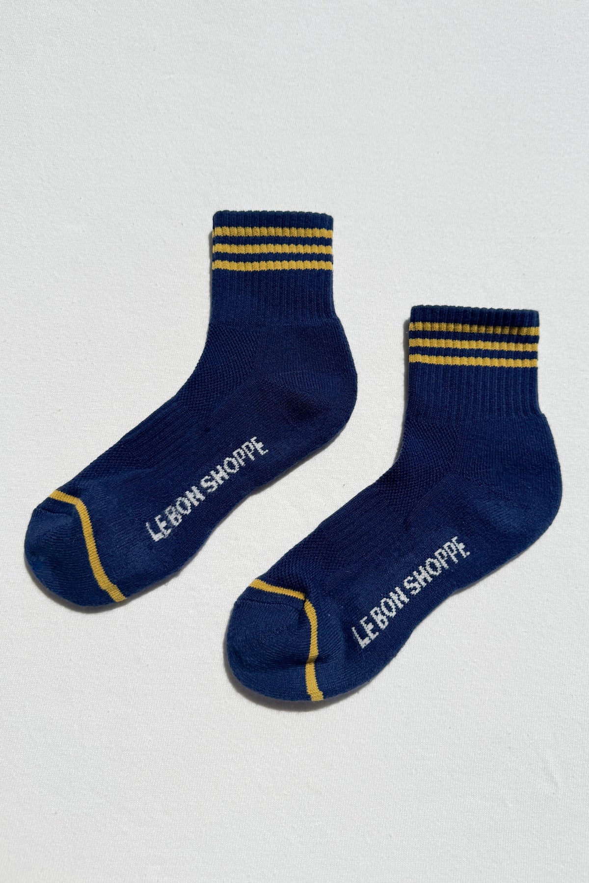 Pair of blue socks with yellow stripes and 'Le Bon Shoppe' branding on a white background
