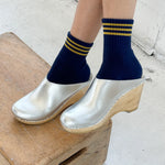 Person wearing navy socks with yellow stripes and silver clogs on a wooden block.