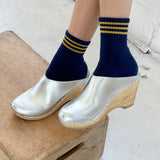 Person wearing navy socks with yellow stripes and silver clogs on a wooden block.