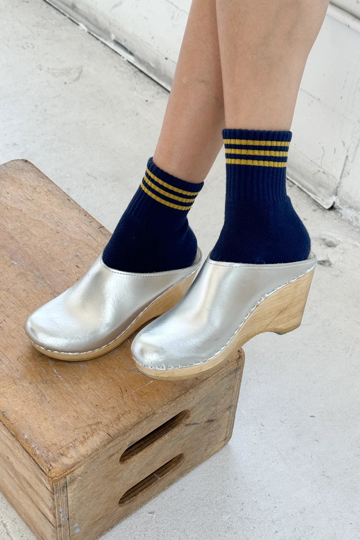 Person wearing navy socks with yellow stripes and silver clogs on a wooden block.