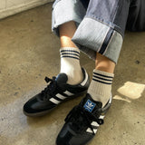 Person wearing black Adidas sneakers with white stripes on a concrete floor.