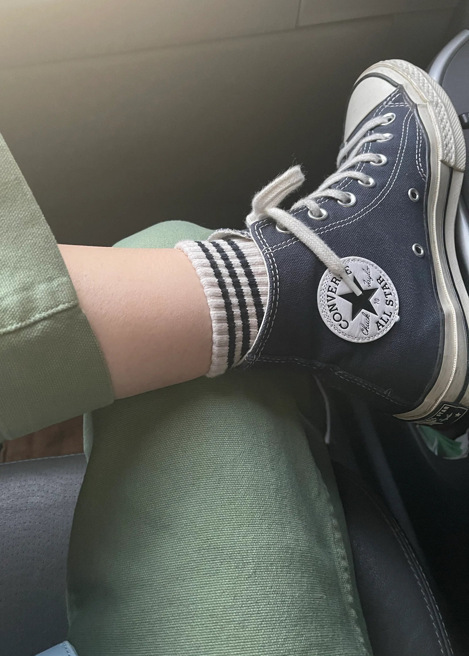 Person wearing navy Converse shoes with white soles sitting inside a vehicle.