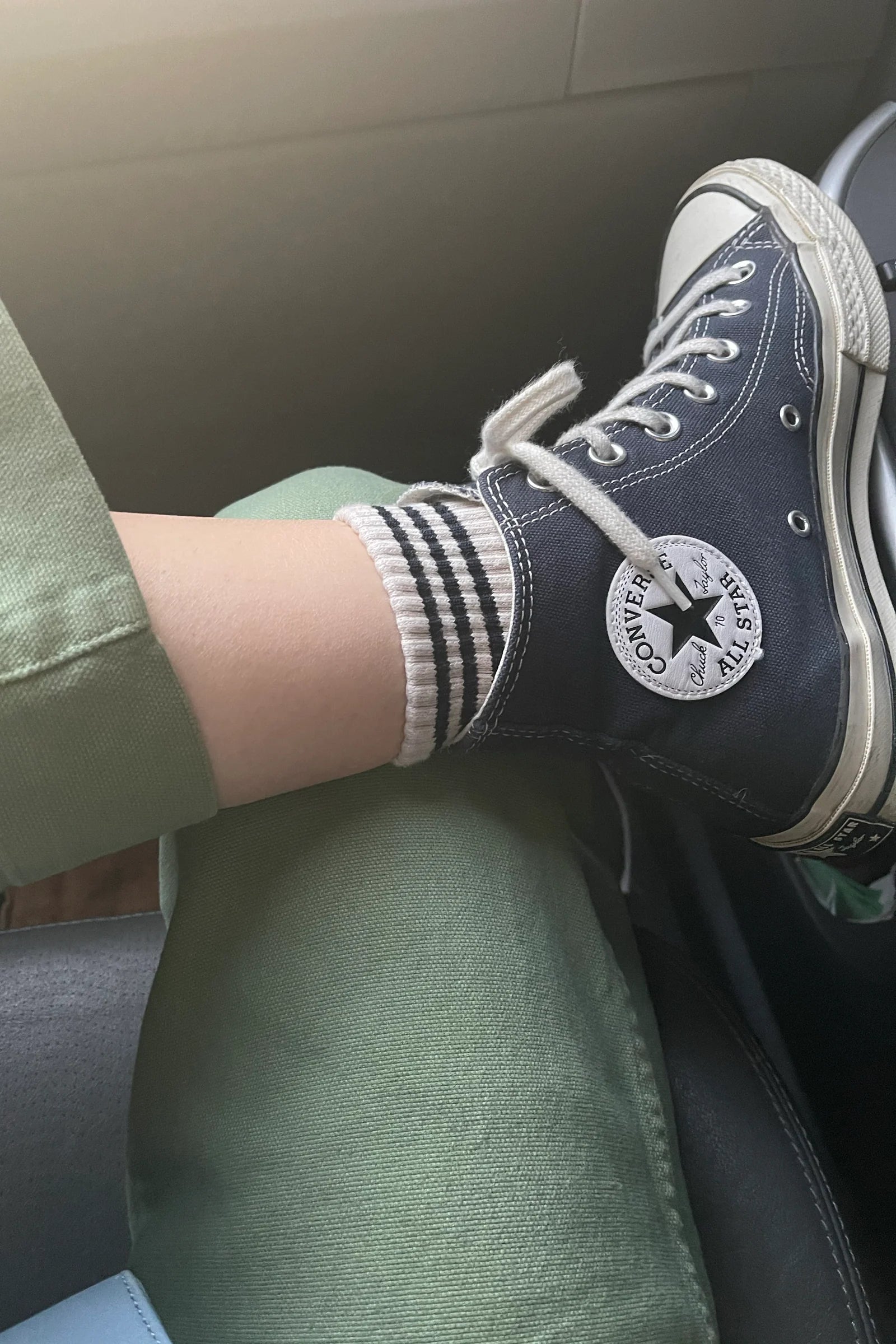 Person wearing navy Converse shoes with white soles sitting inside a vehicle.