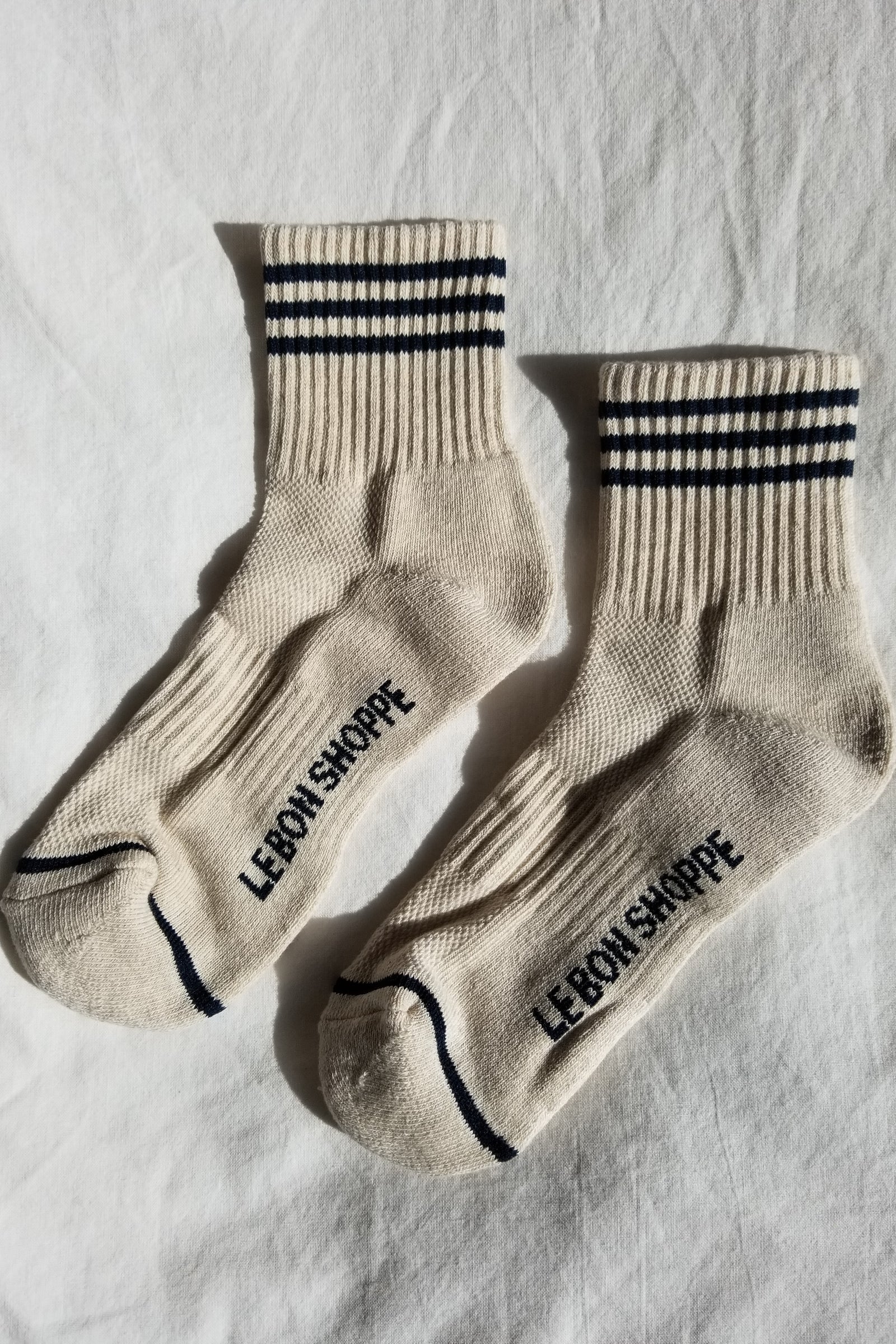 Pair of beige socks with black stripes and text on a light gray background