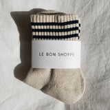 Beige sock with black stripes and 'Le Bon Shoppe' label on a textured gray background