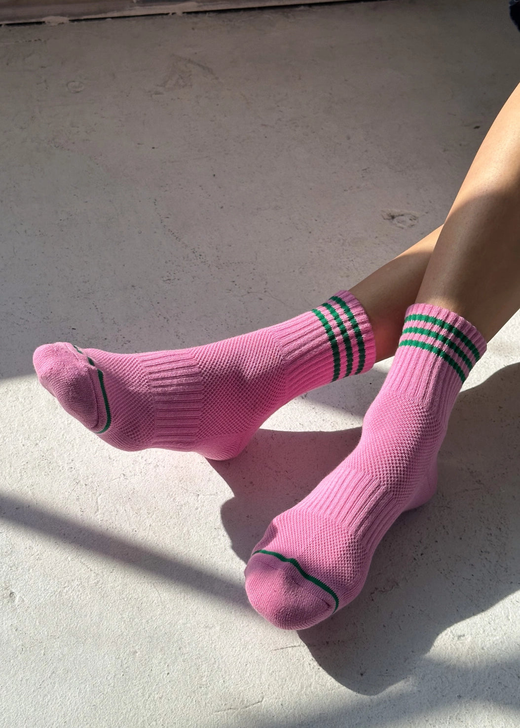 Pink socks with green stripes worn by a person sitting on a concrete surface.