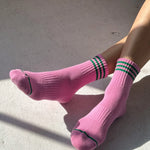 Pink socks with green stripes worn by a person sitting on a concrete surface.