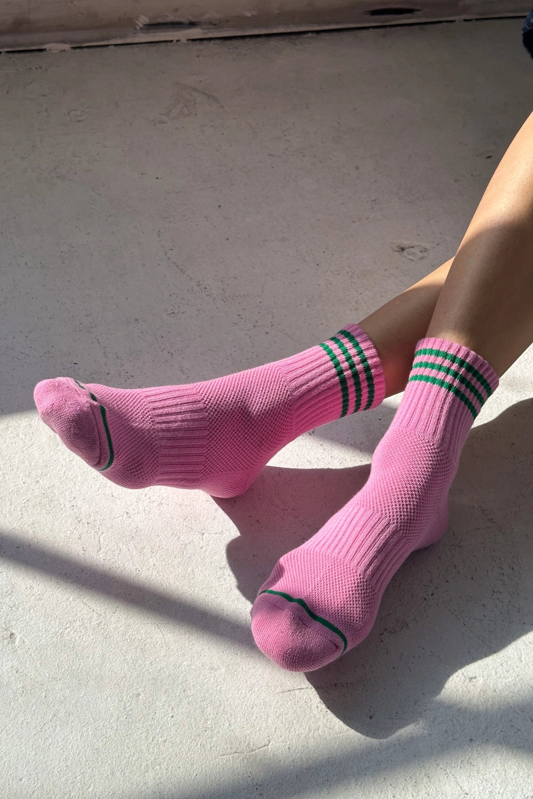 Pink socks with green stripes worn by a person sitting on a concrete surface.