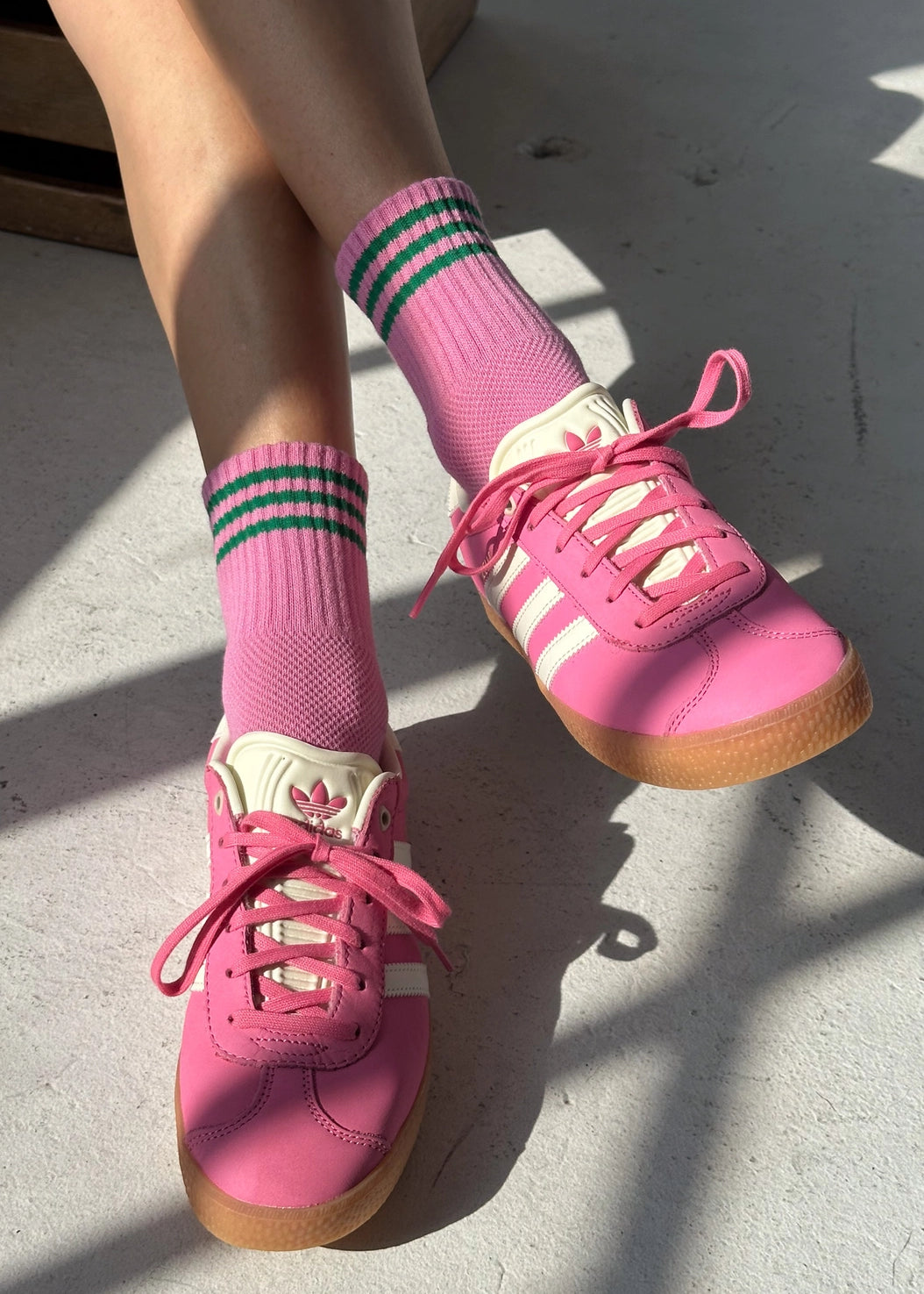 Pink sneakers with white laces and green striped socks on a concrete floor.