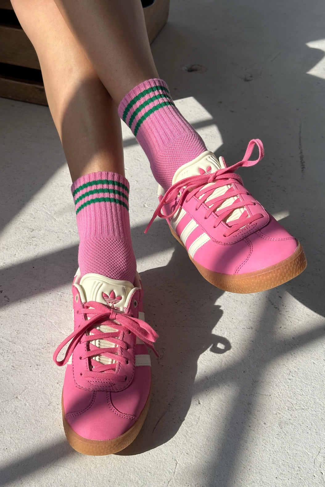 Pink sneakers with white laces and green striped socks on a concrete floor.