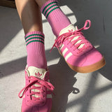 Pink sneakers with white laces and green striped socks on a concrete floor.