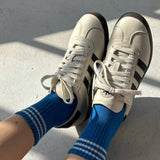 A pair of royal blue ankle crew socks with a white classic crew sock length and a triple contrast stripe at the opening, worn with white sneakers.