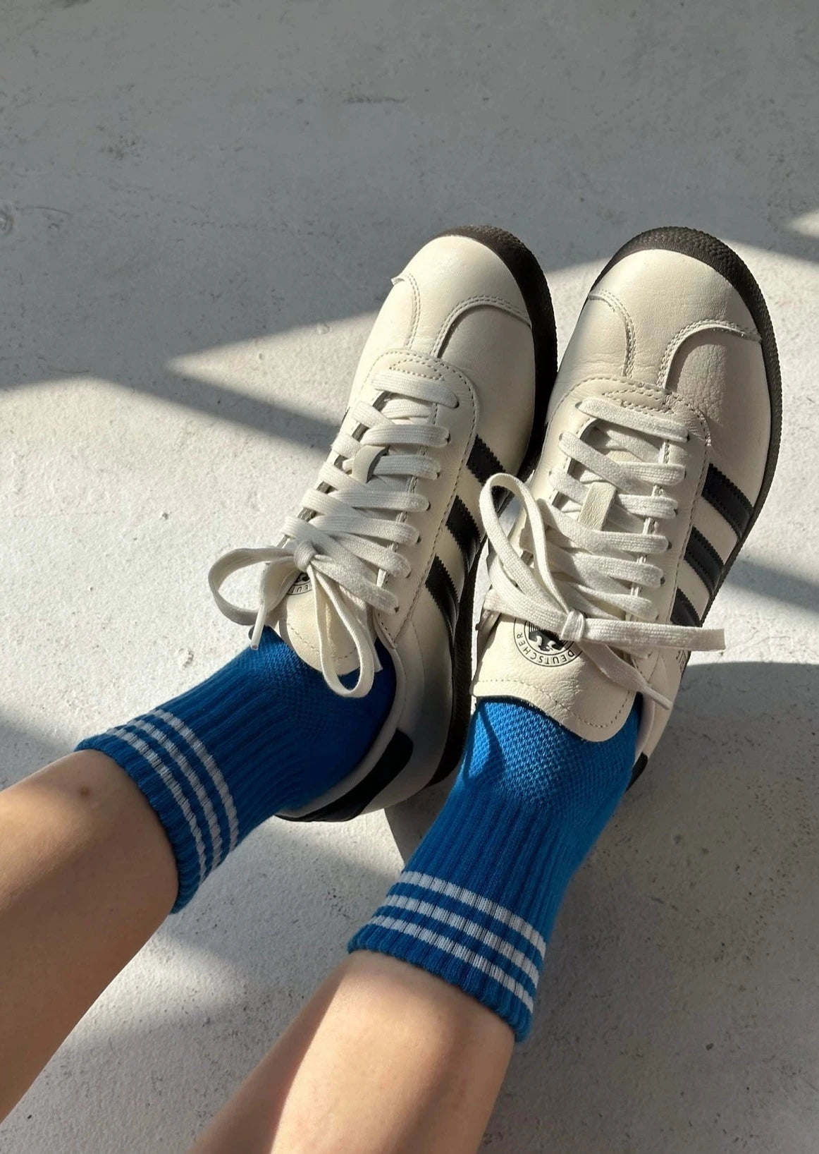 A pair of royal blue ankle crew socks with a white classic crew sock length and a triple contrast stripe at the opening, worn with white sneakers.
