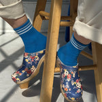 person sitting on a woodd stool wearing blue socks with white stripes and floral clogs