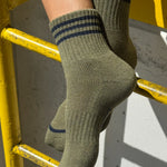 Green socks with blue stripes worn by a person on a yellow metal railing.