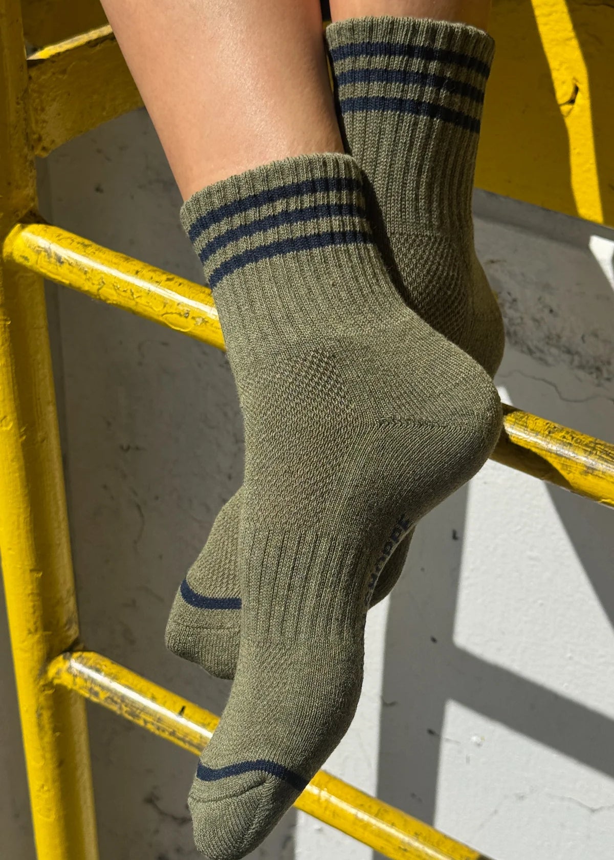 Green socks with blue stripes worn by a person on a yellow metal railing.