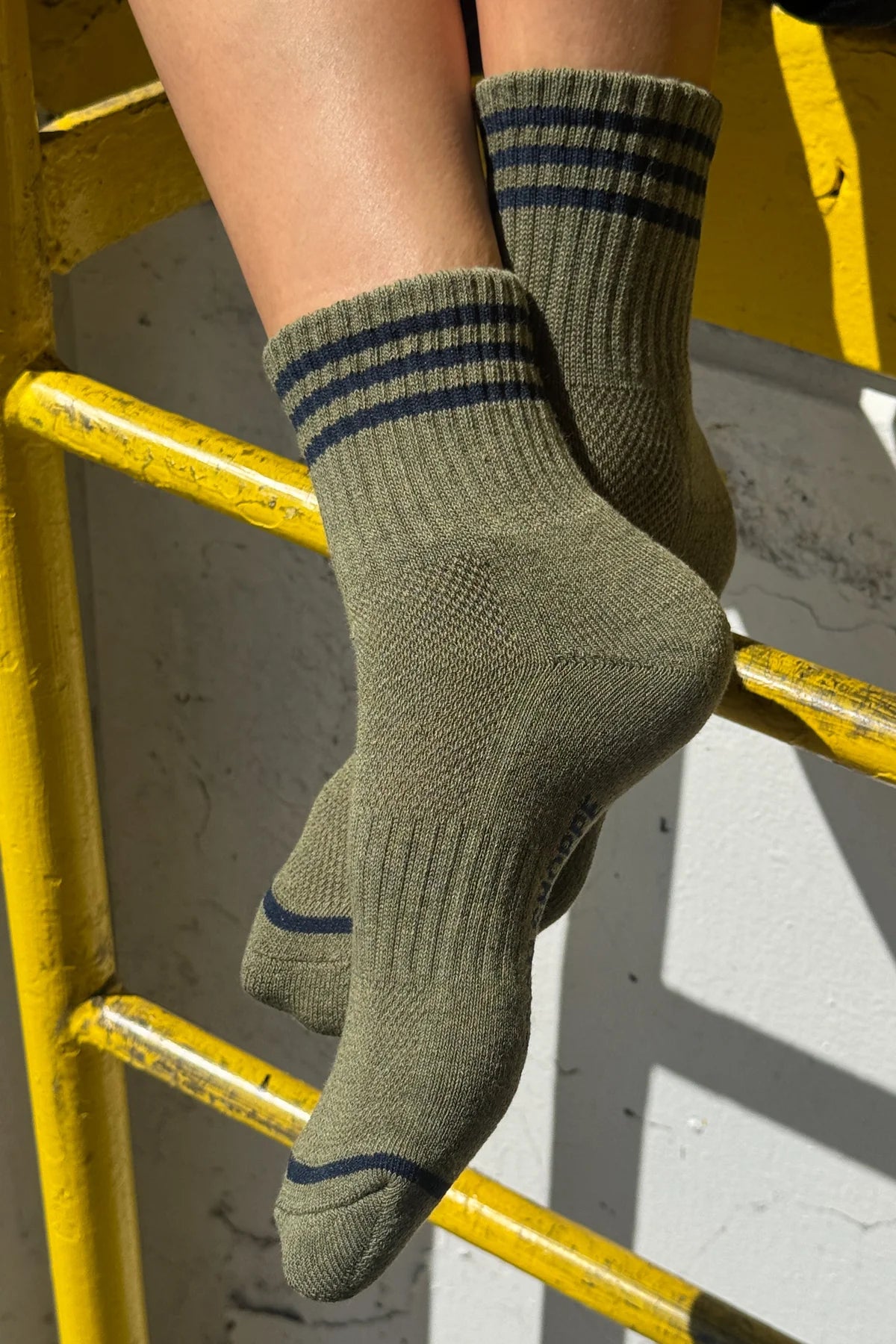 Green socks with blue stripes worn by a person on a yellow metal railing.