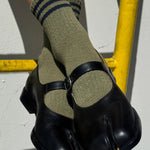 Person wearing green socks with black stripes and black shoes on a gray surface.