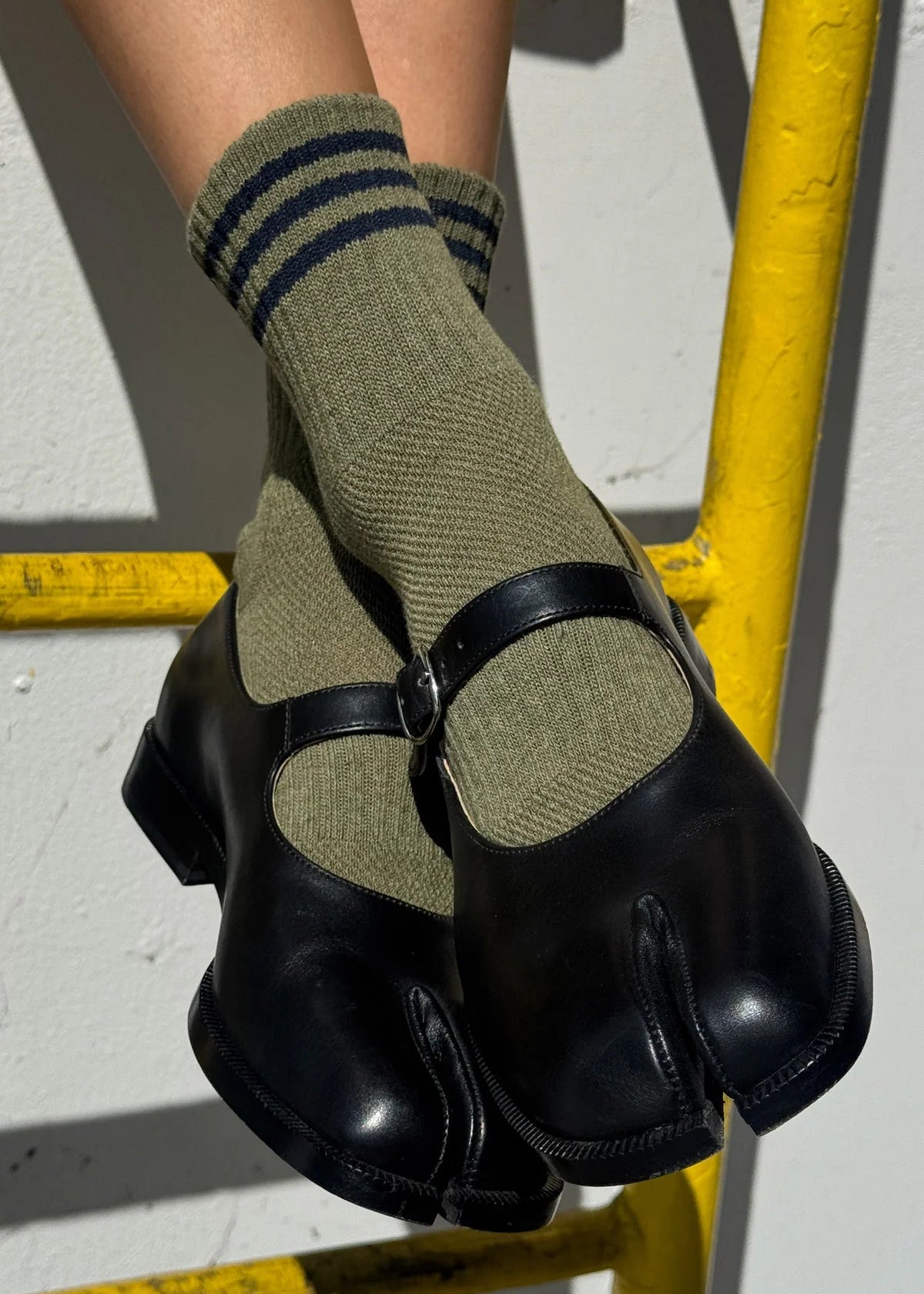Person wearing green socks with black stripes and black shoes on a gray surface.
