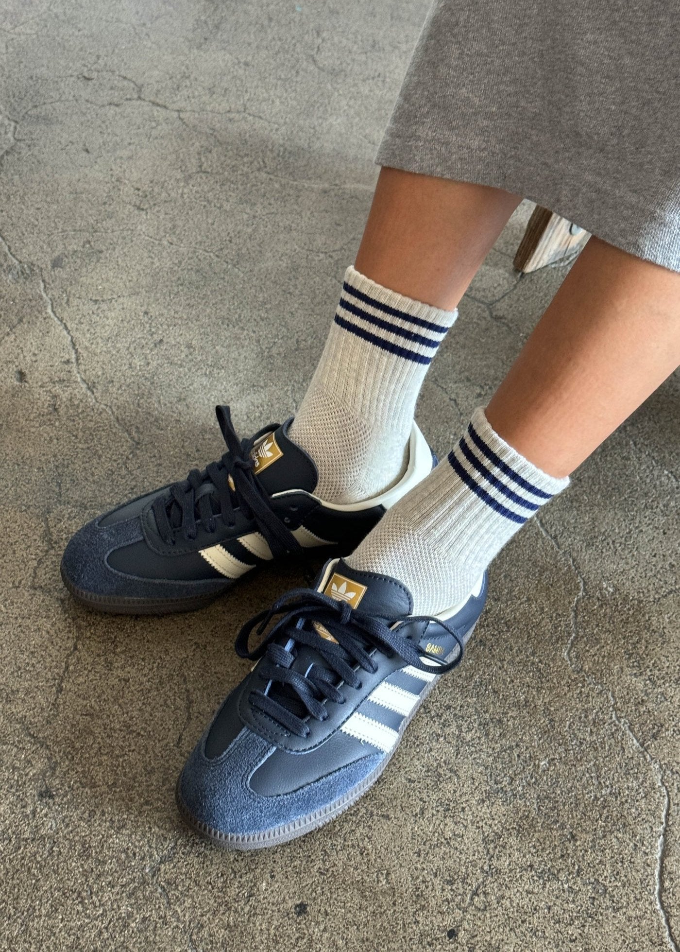 A pair of white ankle socks with a blue  stripes at the opening, worn with gray sneakers.