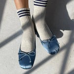 Person wearing oatmeal socks with blue stripes and blue ballet slippers with bows on light grey floor