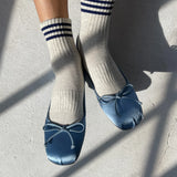 Person wearing oatmeal socks with blue stripes and blue ballet slippers with bows on light grey floor
