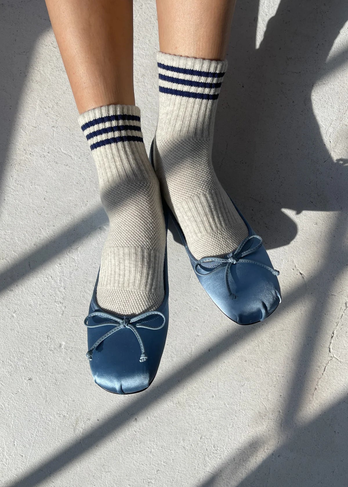 Person wearing oatmeal socks with blue stripes and blue ballet slippers with bows on light grey floor