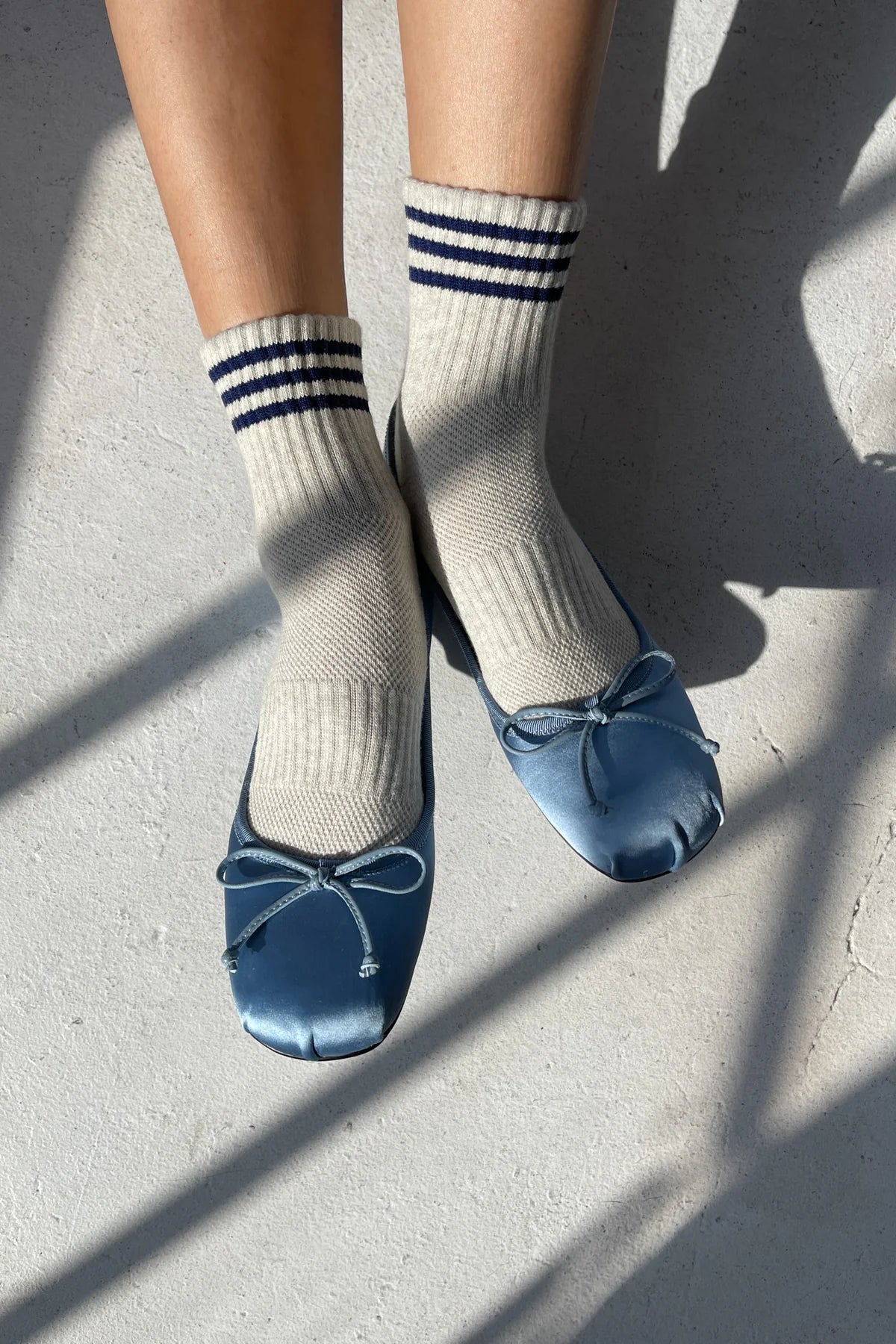 Person wearing oatmeal socks with blue stripes and blue ballet slippers with bows on light grey floor