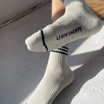 Person wearing oatmeal socks with blue stripes and Le Bon Shoppe branding on light grey background