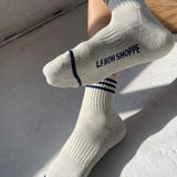 Person wearing oatmeal socks with blue stripes and Le Bon Shoppe branding on light grey background