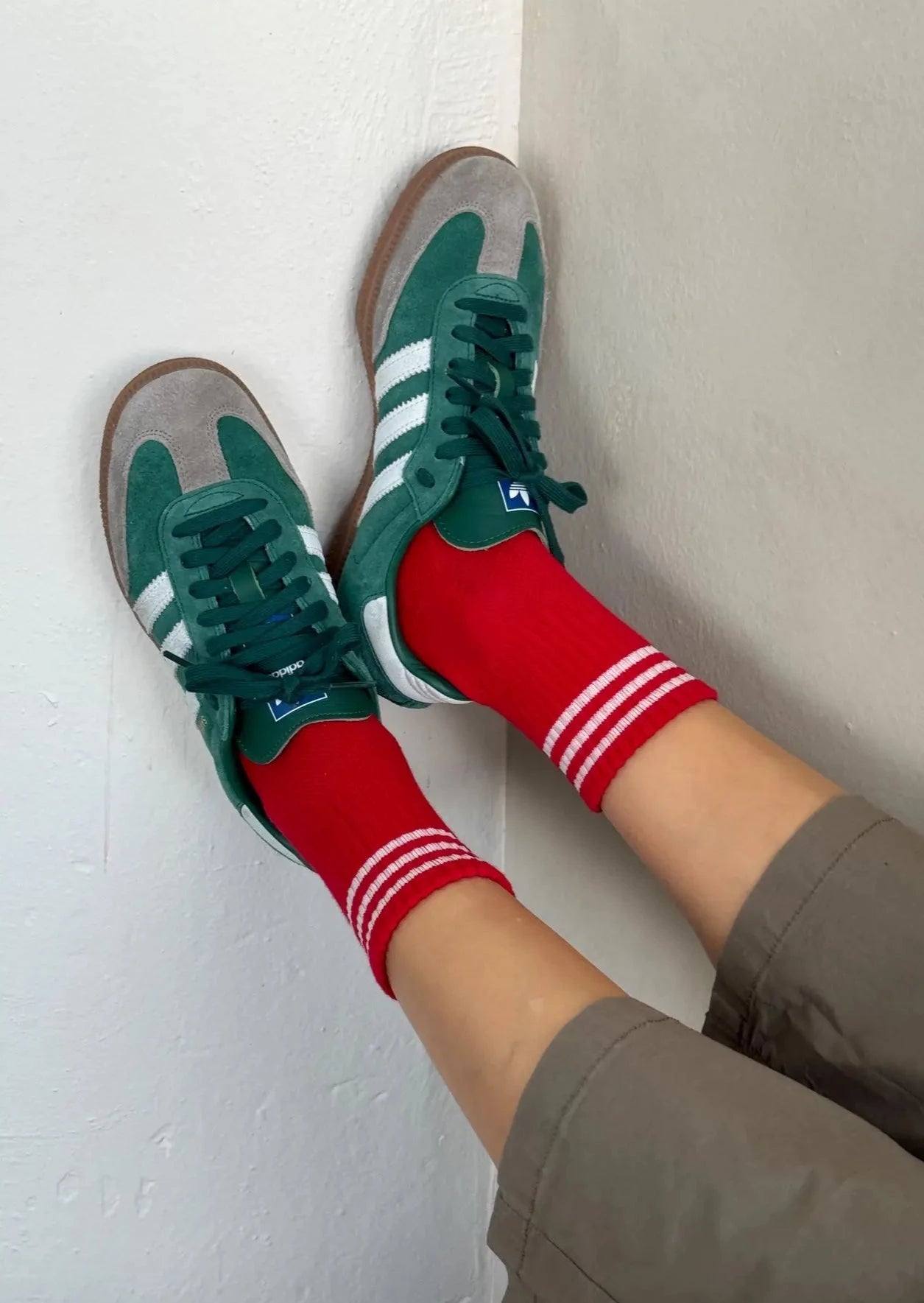 A pair of red ankle crew socks with white and green stripes at the heel and toe, worn with green sneakers.