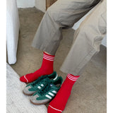Person wearing grey pants andred socks with white stripes . There are green sneakers between their feet.