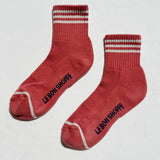Red socks with white stripes and 'Le Bon Shoppe' branding on a light gray background