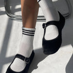 Black shoes with white socks featuring three black stripes on a light background