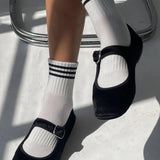 Black shoes with white socks featuring three black stripes on a light background