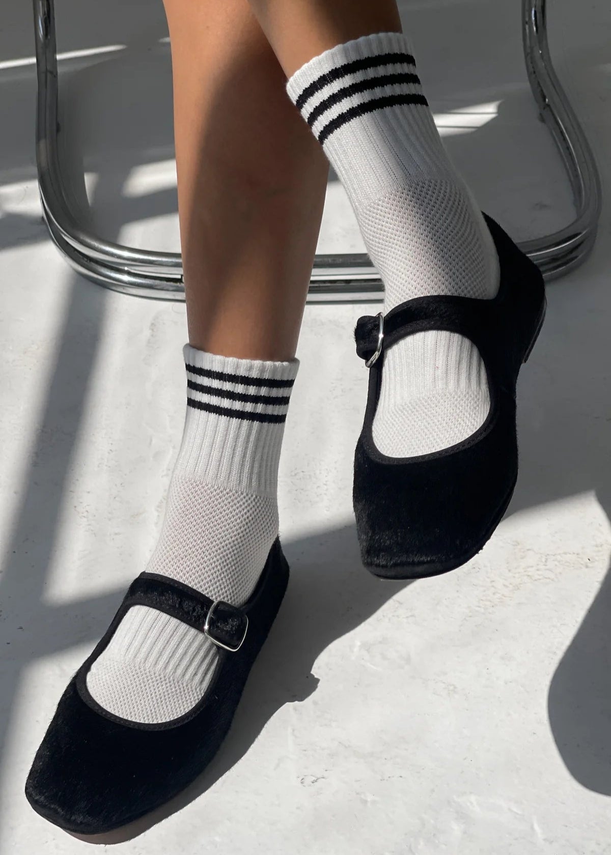 Black shoes with white socks featuring three black stripes on a light background