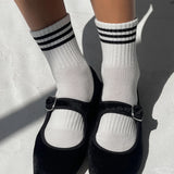 Black shoes with white socks featuring three stripes on a light background