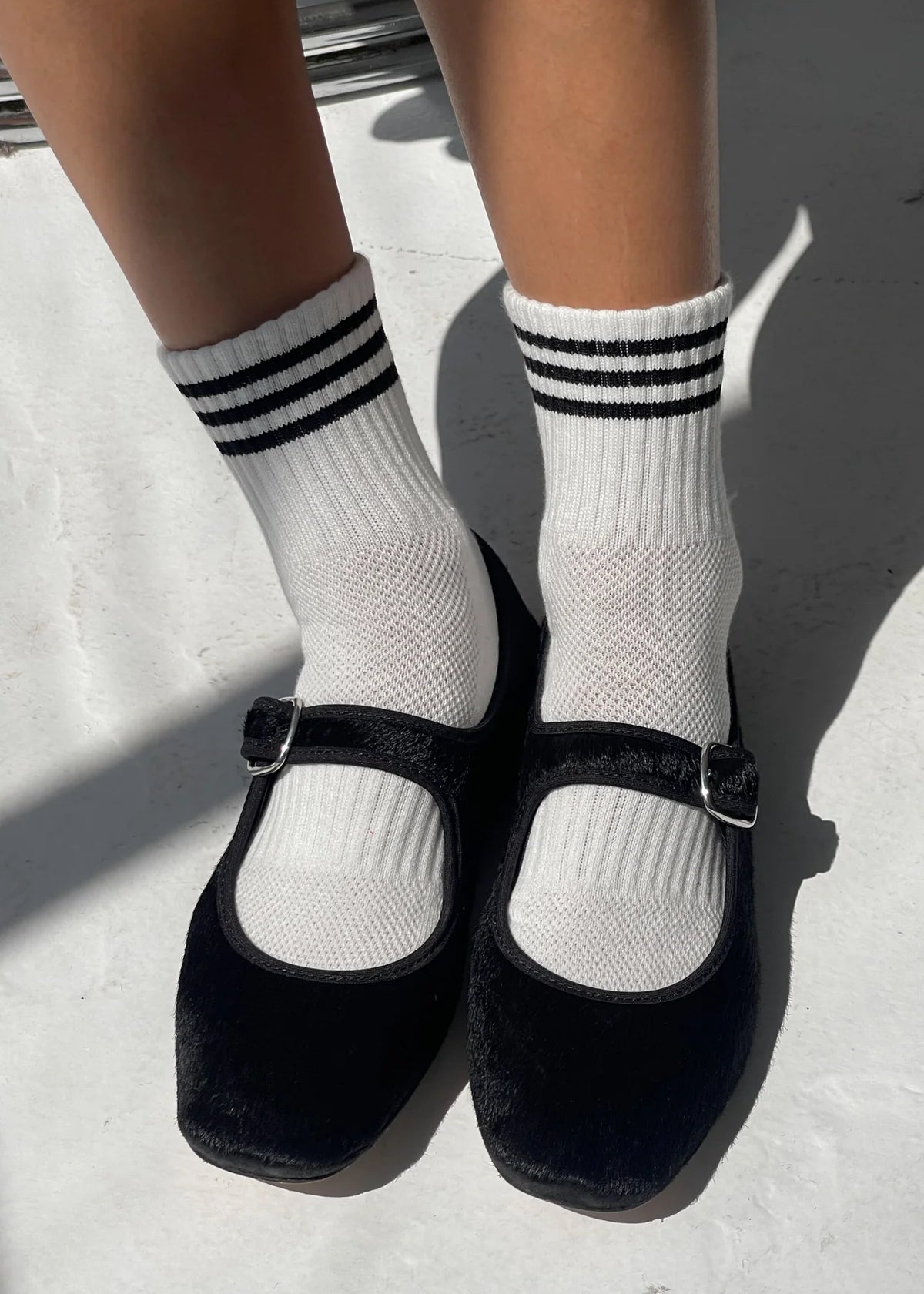 Black shoes with white socks featuring three stripes on a light background