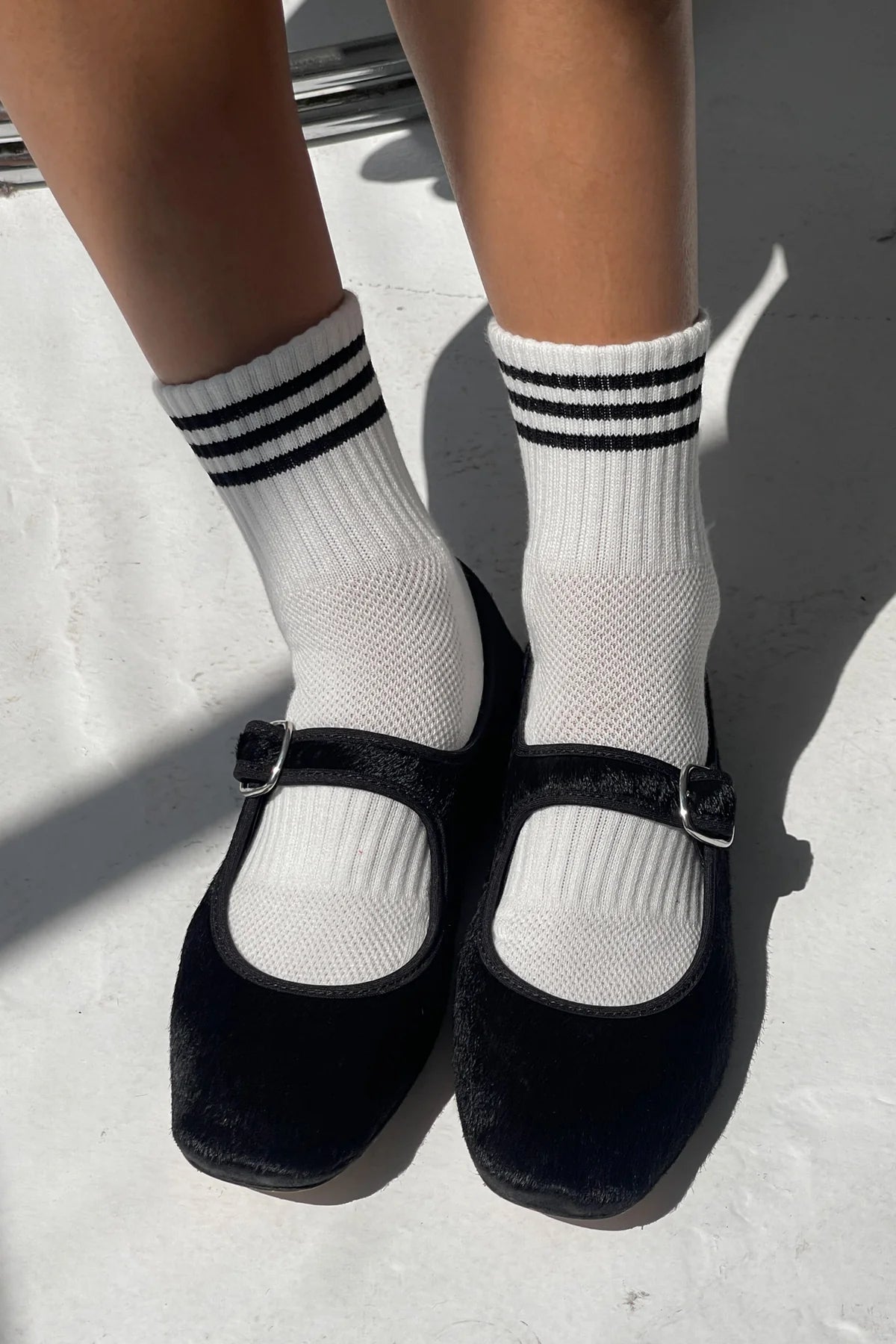 Black shoes with white socks featuring three stripes on a light background