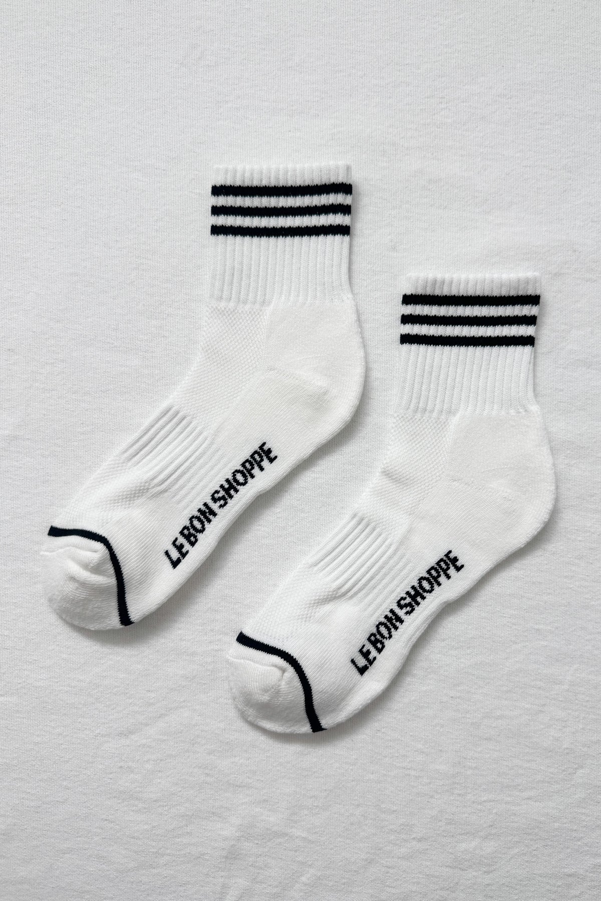 White socks with black stripes and 'LE BON SHOPPE' text on a light gray background
