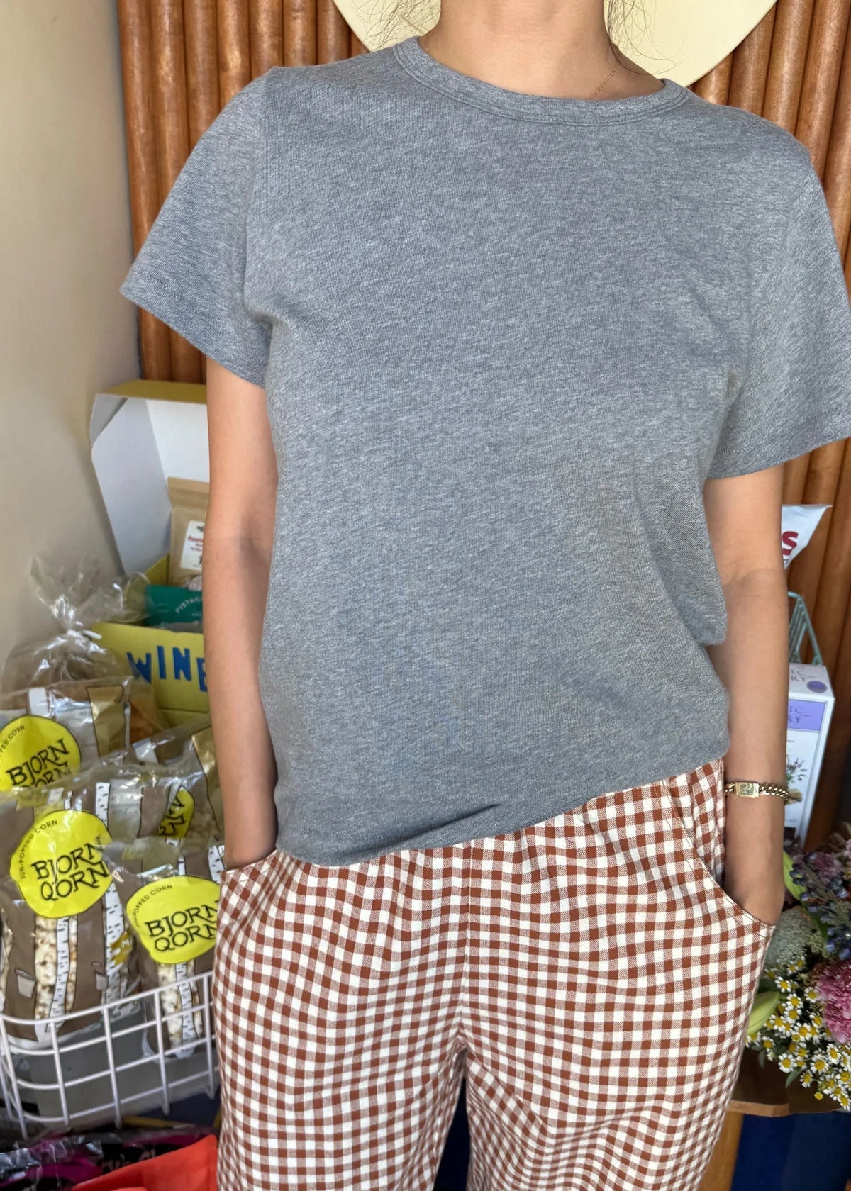 Person wearing a gray t-shirt and checkered pants standing in front of a store shelf.
