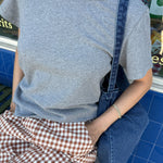 Person wearing a gray t-shirt and denim overalls sitting on a bench.
