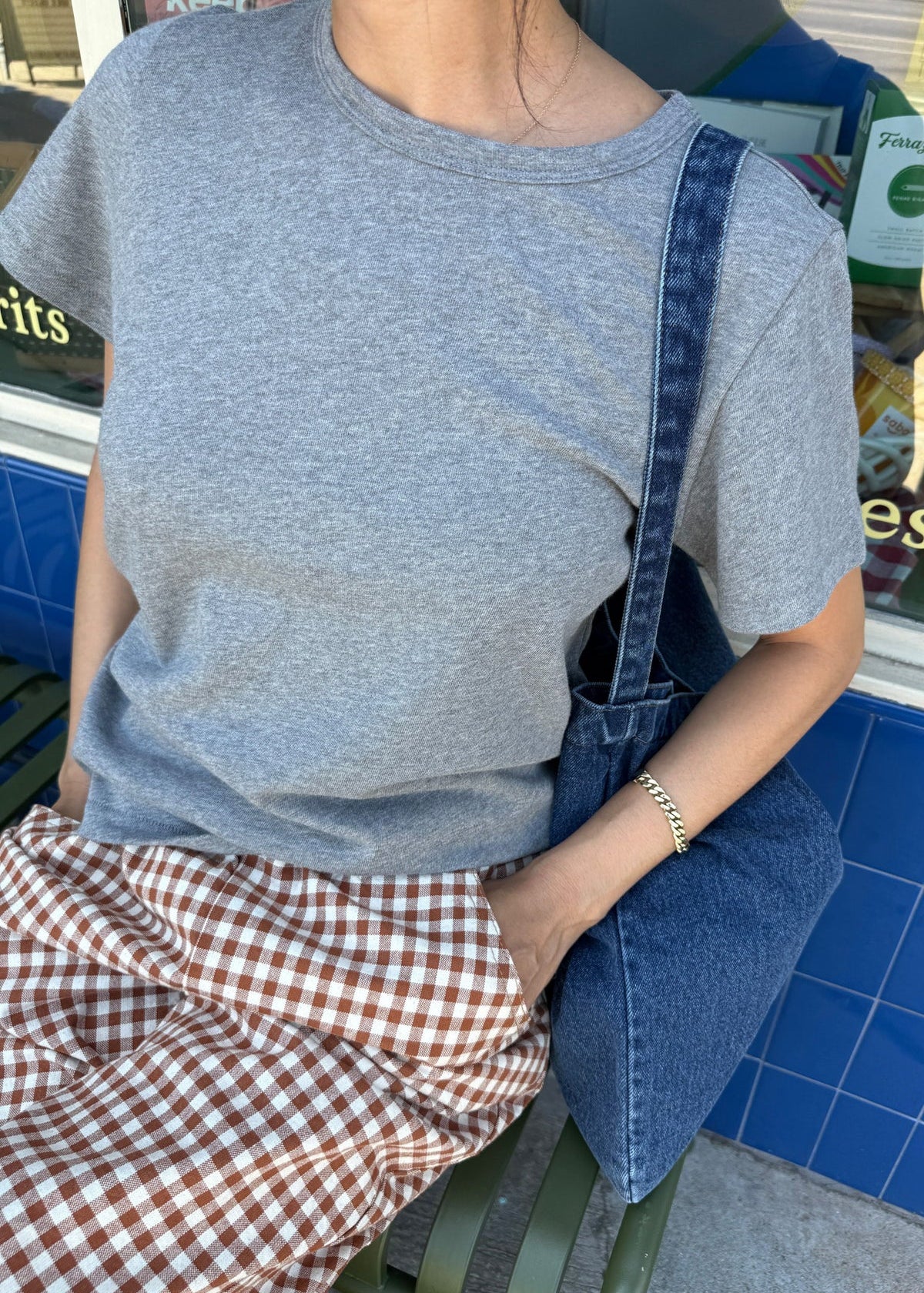 Person wearing a gray t-shirt and denim overalls sitting on a bench.