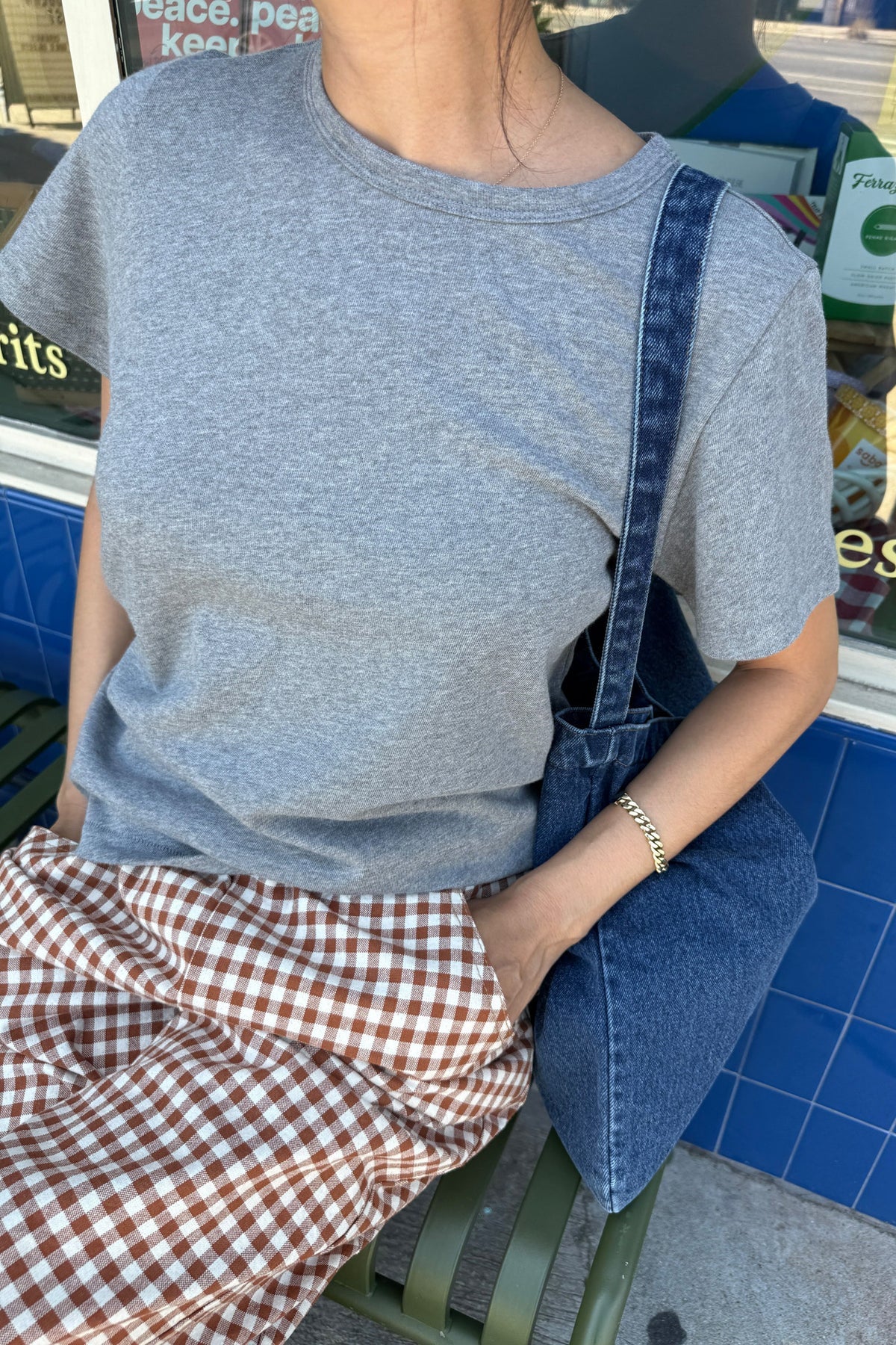 Person wearing a gray t-shirt and denim overalls sitting on a bench.
