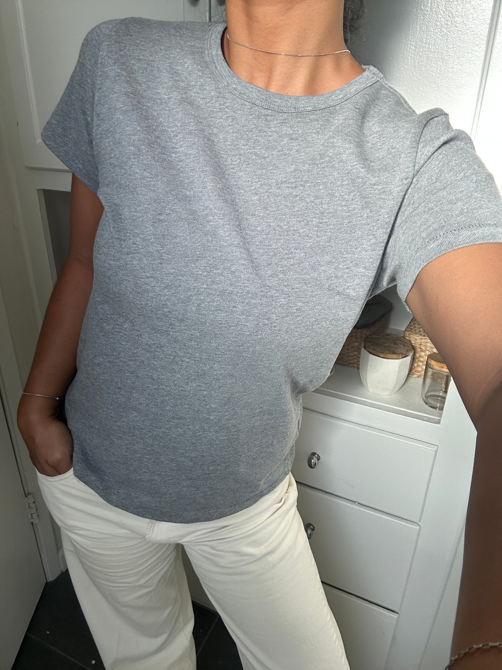 Person wearing a gray t-shirt and white pants in a room with a white cabinet.