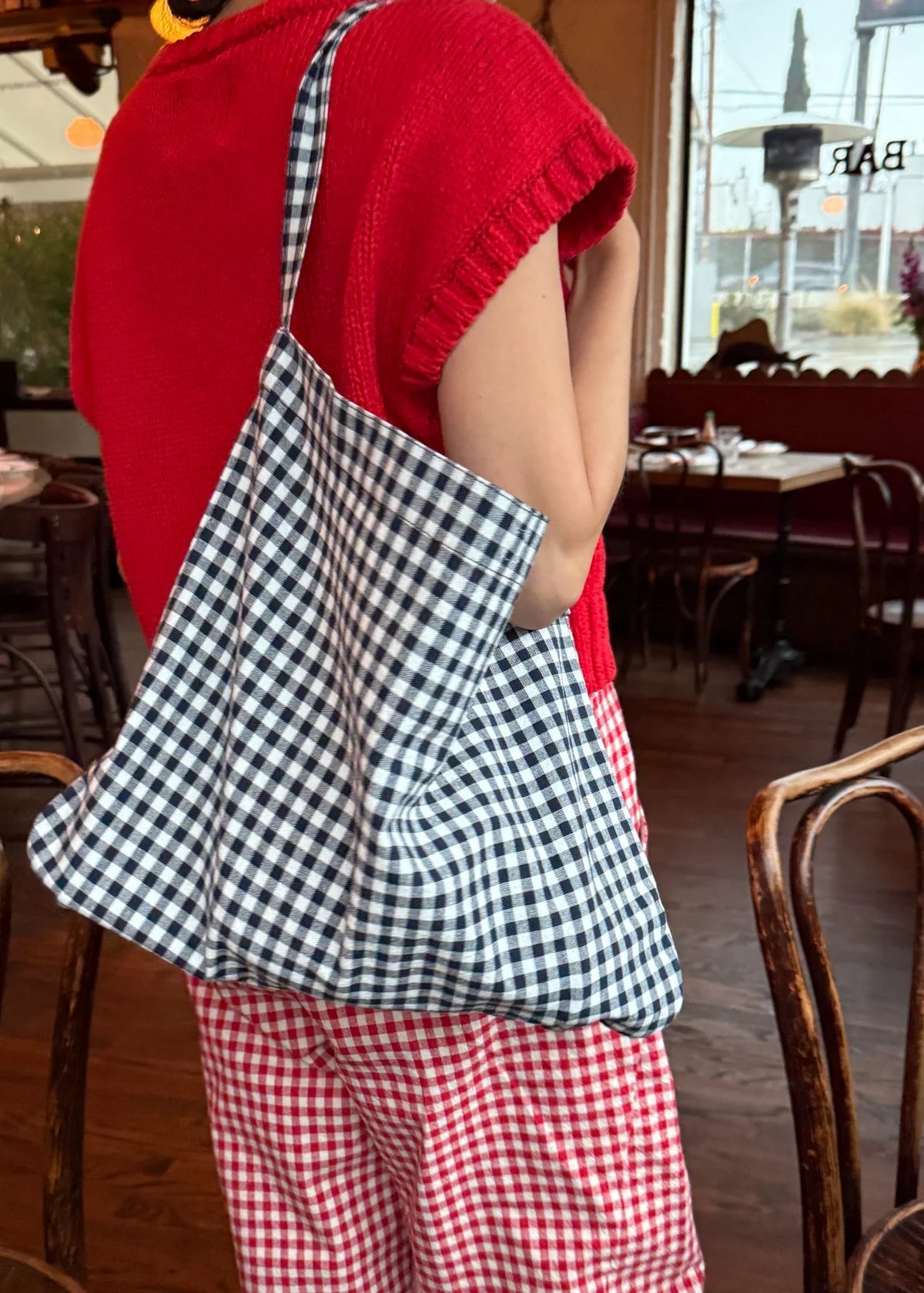 Person wearing a red outfit with a checkered bag in a restaurant setting